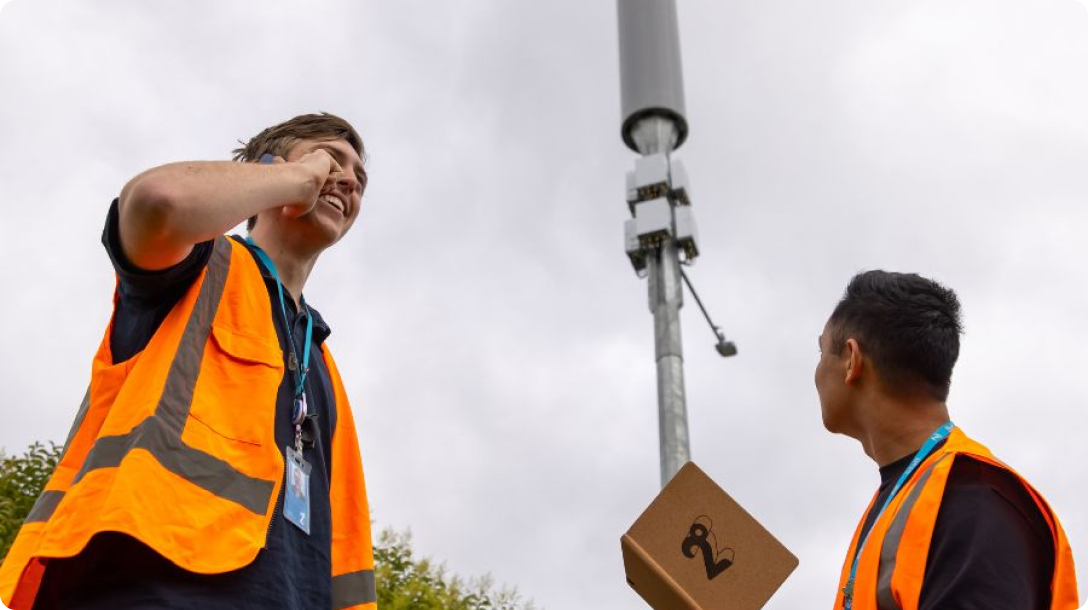 Photo of engineers one looking at a cell tower and one taking a call