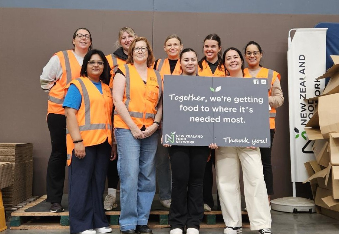 Group photo of workers for the New Zealand Food Network holding a sign that says "Together, we're getting food to where it's needed most."